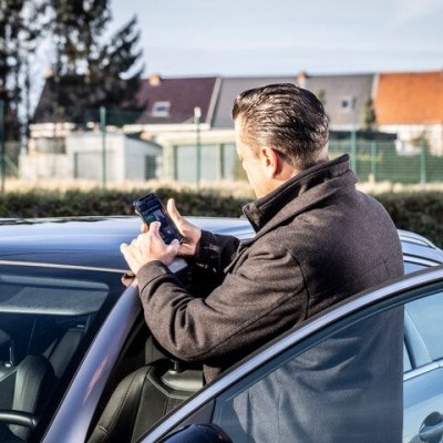 man op gsm naast auto