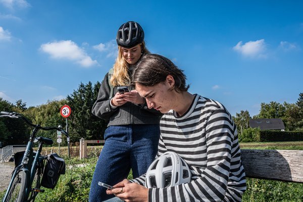jongeren op hun gsm op een bankje naast de fiets
