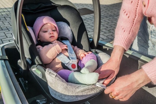 moeder die baby veilig vastmaakt met gordeltjes in een autostoeltje